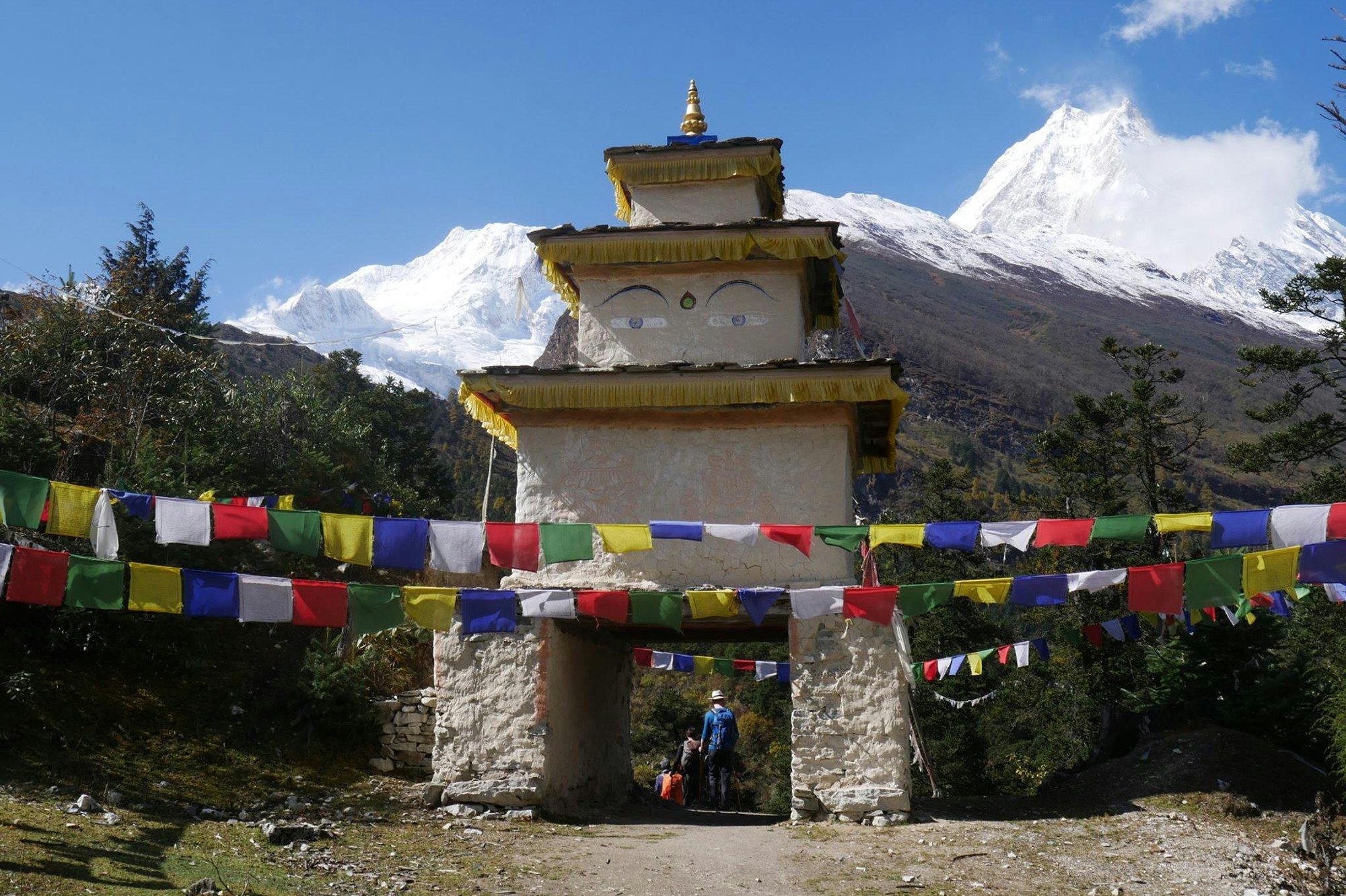 A stupa with Buddha eyes painted on and prayer flags in the foreground